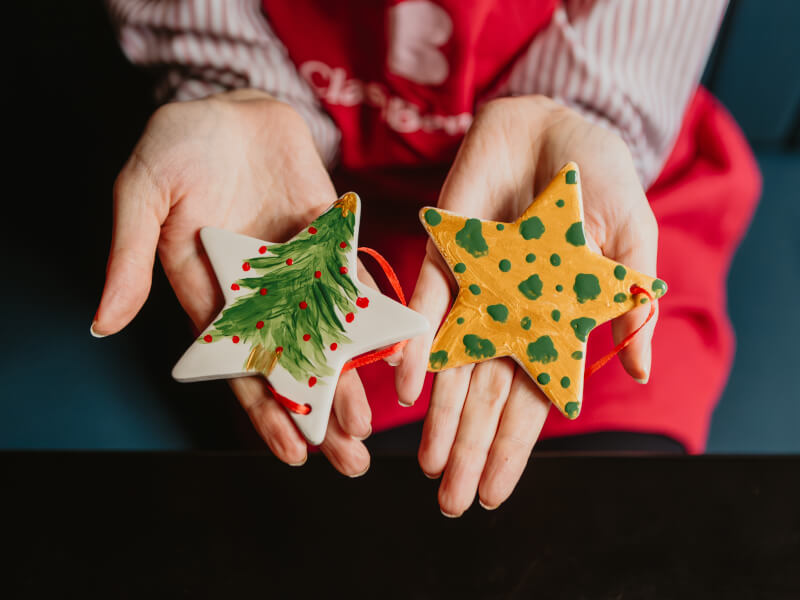 Two hands outstretched, holding handpainted star shaped Christmas ornaments